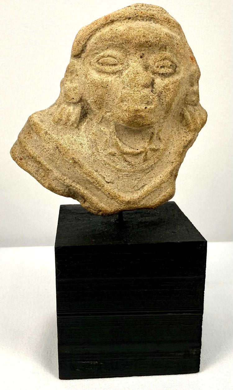 Frontal view of Ancient Terracotta Figure Fragment with almond eyes and parted lips on black stand