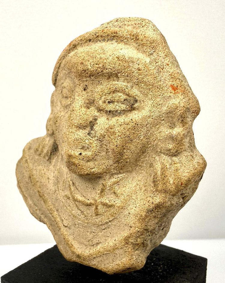 Angled view of weathered light brown clay sculpture fragment showing broad face and broken edges