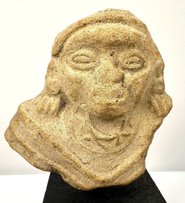 Close-up of sandy-colored terracotta bust highlighting molded oval eyes, nose, and neck details