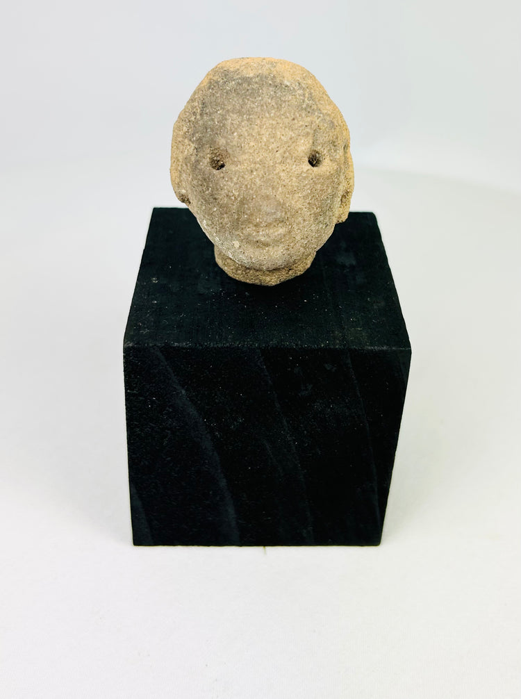 Terracotta head fragment, West Mexico, Pre-Columbian era, with drilled eyes and soft facial features, circa 300 BCE–300 CE, on black display stand
