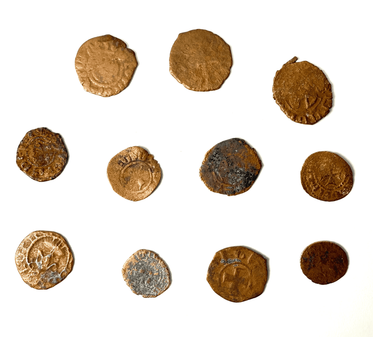 Eleven medieval copper-alloy coins with varying diameters, reddish-brown surfaces, and localized green oxidation.