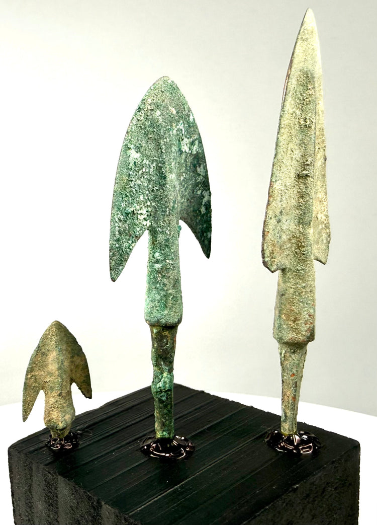 Compact bronze barbed arrowhead featuring a triangular blade, swallowtail-shaped shoulders, and pale green mineral deposits.
