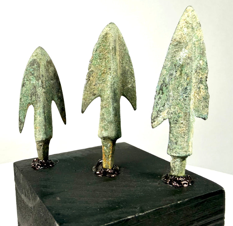 Three ancient bronze projectile points with green patina on black display stand