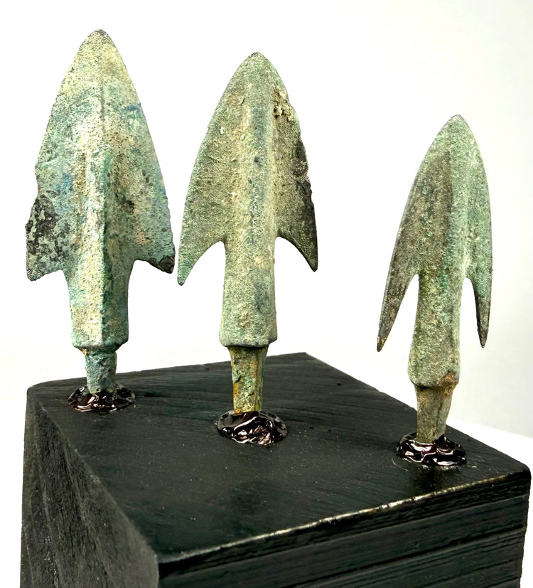 Rear view of cast bronze arrowheads showing cylindrical tangs and oxidation