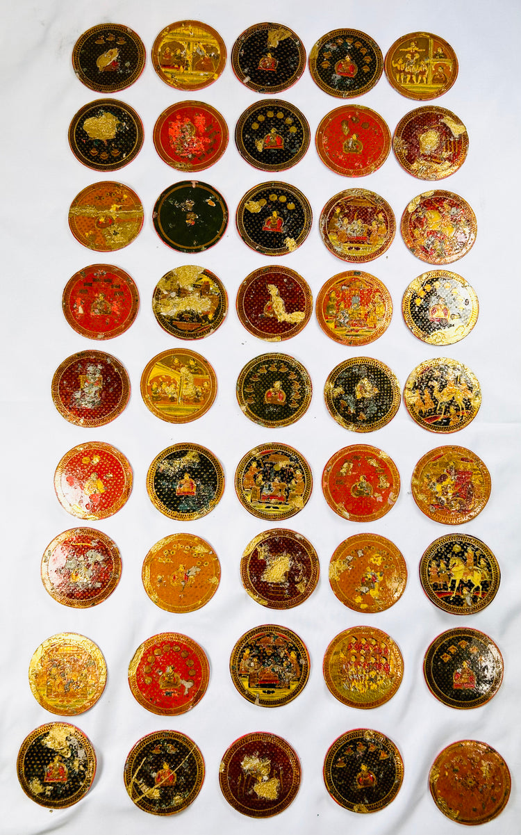 Large arrangement of 19th-century Indian Ganjifa playing cards showing diverse miniature painted scenes on circular lacquered cards, displayed on a white background.