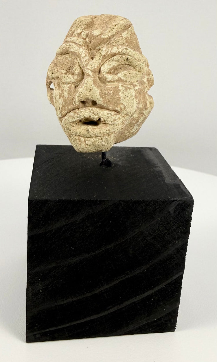 Ancient Mesopotamian-style carved stone head fragment featuring almond-shaped eyes, a broad nose, and a simplified mouth.