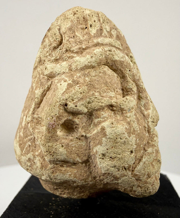 Frontal close-up of carved limestone face with abstract geometric features and heavy brows