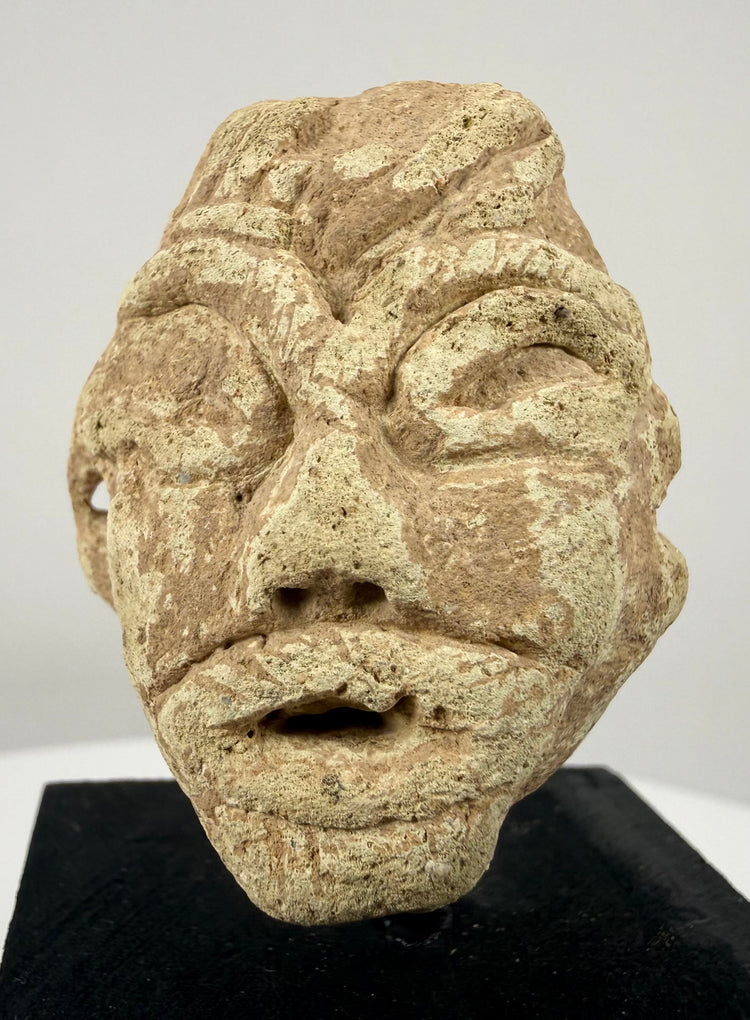 Ancient Mesopotamian-style stone sculpture featuring deeply incised eyes, geometric facial details, and a weathered surface.