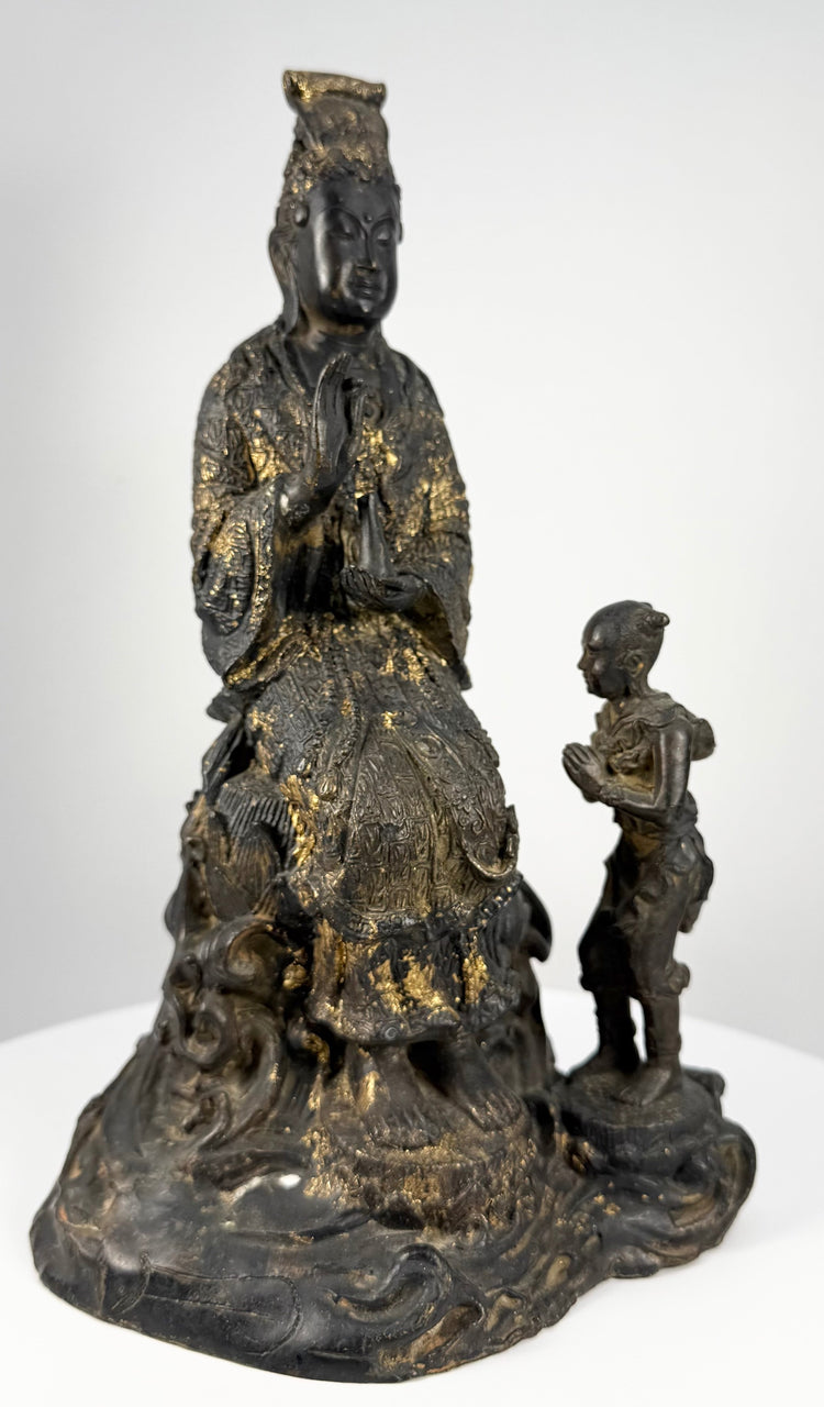 Antique Thai Buddhist sculpture depicting Guanyin seated on an elaborate lotus pedestal beside a small child attendant.