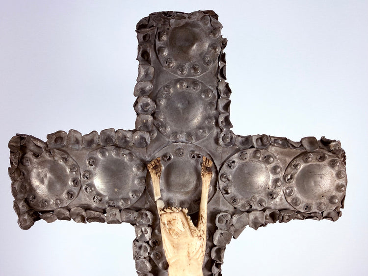 Close-up of embossed tin medallions and upper bone figure on antique cross