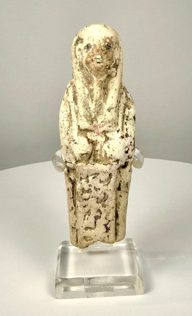 Limestone ushabti figure with a carved tripartite wig extending over the shoulders and framing the stylized facial features.