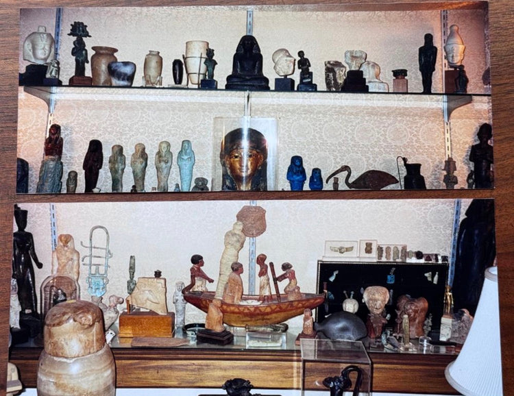 Historical collection photograph from Dr. Bruce L. Ralston’s private collection in Tuxedo Park, New York, showing the Egyptian faience ushabti positioned beneath a large Egyptian boat model among other antiquities, circa late 1970s–1980s.