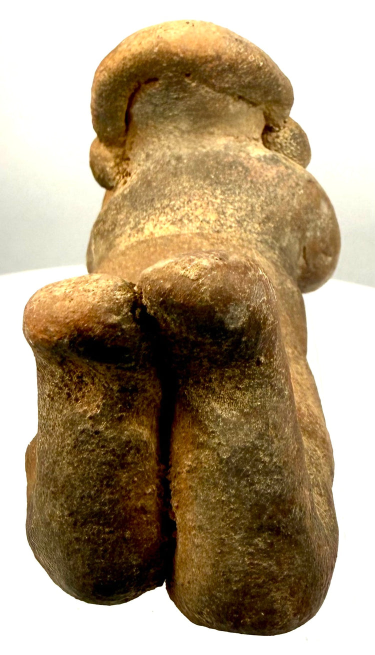 Pre-Columbian terracotta prone human figure with distinctive pierced earspools, rounded facial features, elongated limbs, and surviving sculptural details.