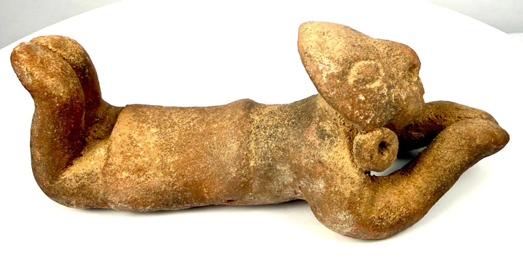 Pre-Columbian terracotta prone figure with both arms extended forward, rounded hands, and legs raised behind the elongated body.