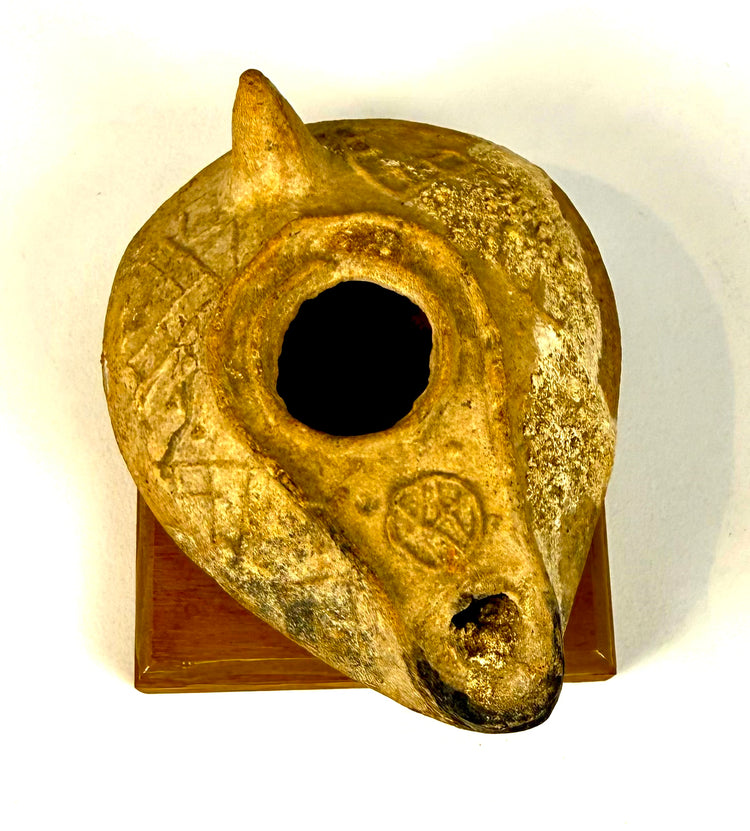 Ancient terracotta oil lamp featuring a conical rear handle, rounded filling opening, and darkened wick aperture from historical use.