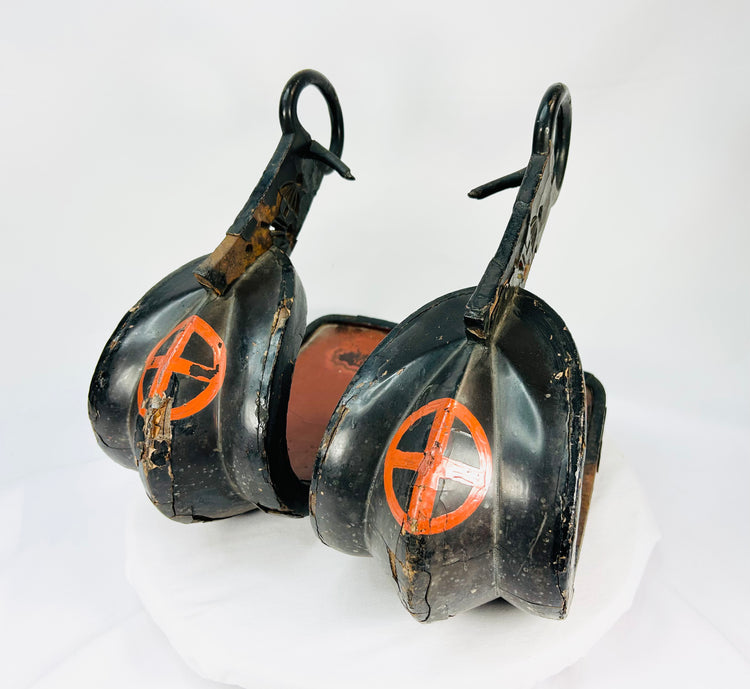 Close-up view of a pair of antique Japanese lacquered samurai stirrups from the Edo–Meiji period, featuring black lacquer with red cross-in-circle mon crests, displayed on a white background.