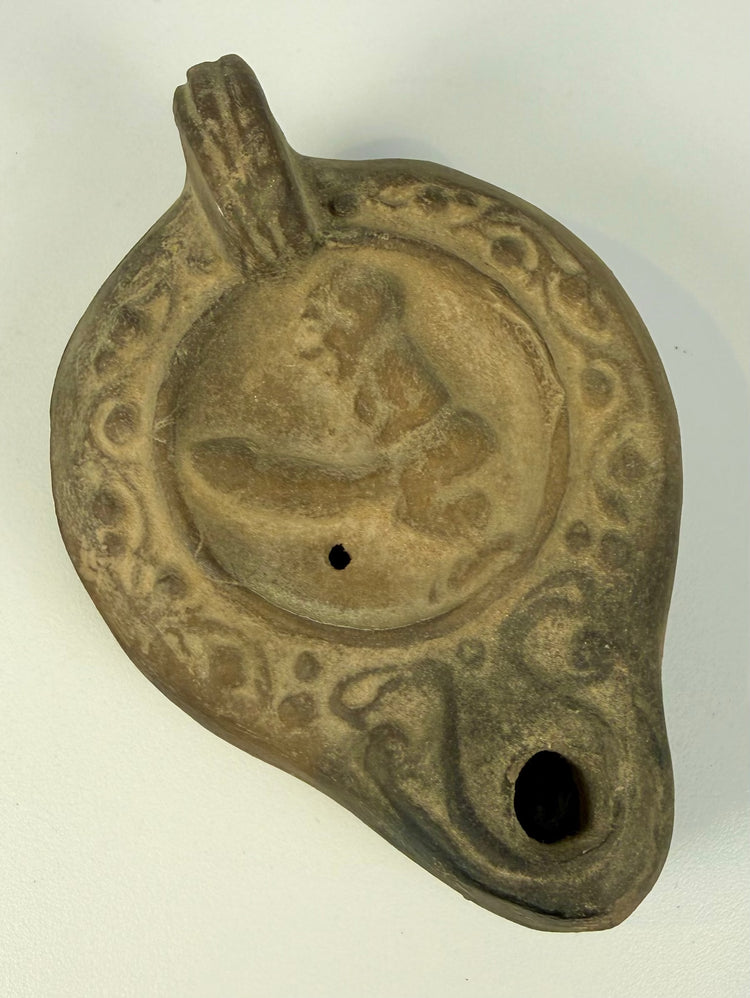Ancient Roman erotic terracotta lamp with a detailed figural composition surrounded by decorative scrolling and geometric patterns.