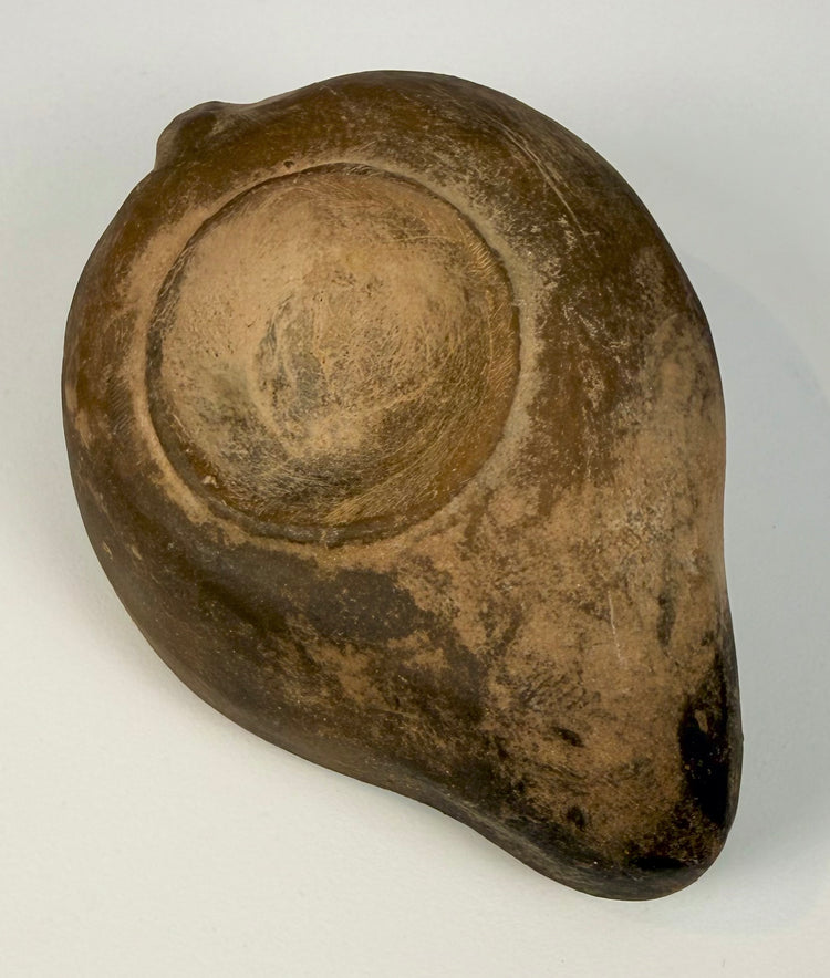 Ancient Roman ithyphallic oil lamp with an upright rear lug handle, rounded nozzle, and weathered earthenware surface.