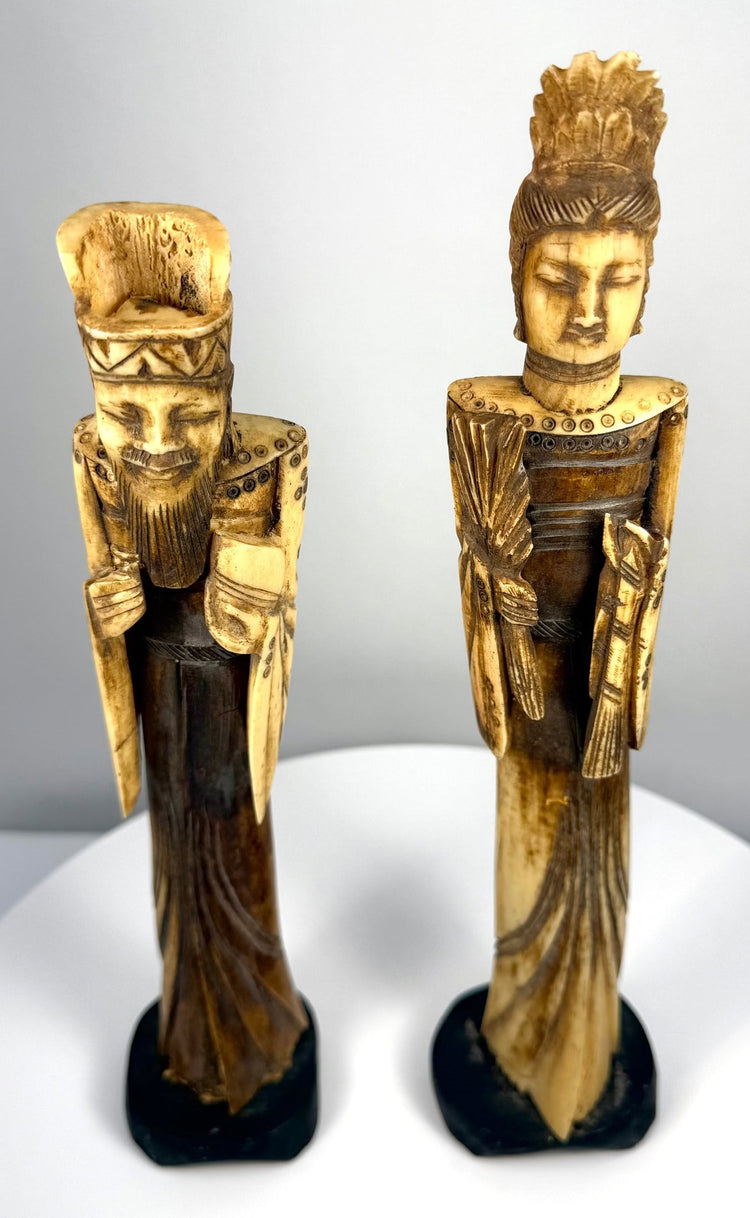 Matched Chinese Emperor and Empress figurines mounted on individual black display bases, featuring visible natural bone texture, dark staining, and vintage surface wear.