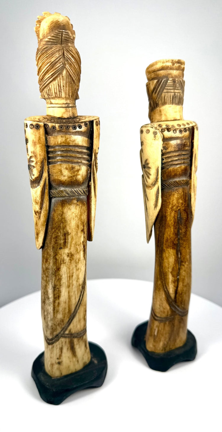 Vintage Chinese bone sculptures displaying dark-stained central sections, pale carved faces, ornamental accessories, and aged surface coloration.