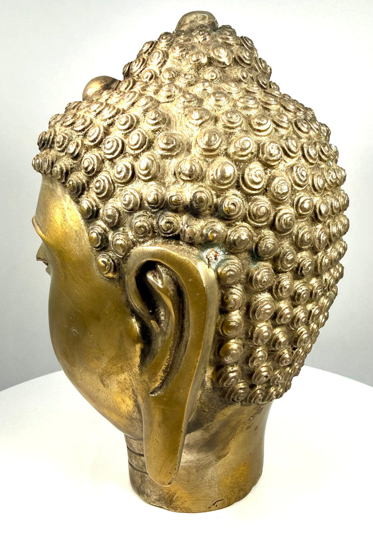 Antique-style cast-metal Buddha head featuring warm brass-like highlights, darker oxidation, and textured patination within the recessed sculptural details.