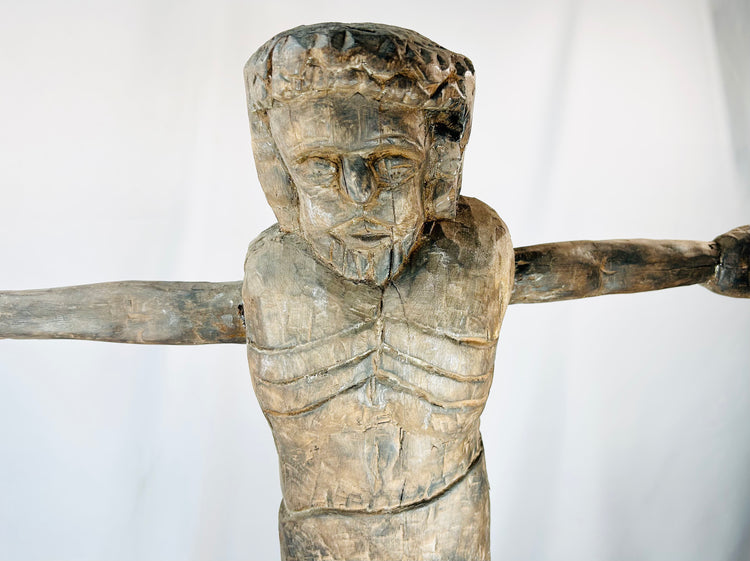 Religious wooden sculpture of Christ in cruciform pose with visible tool marks