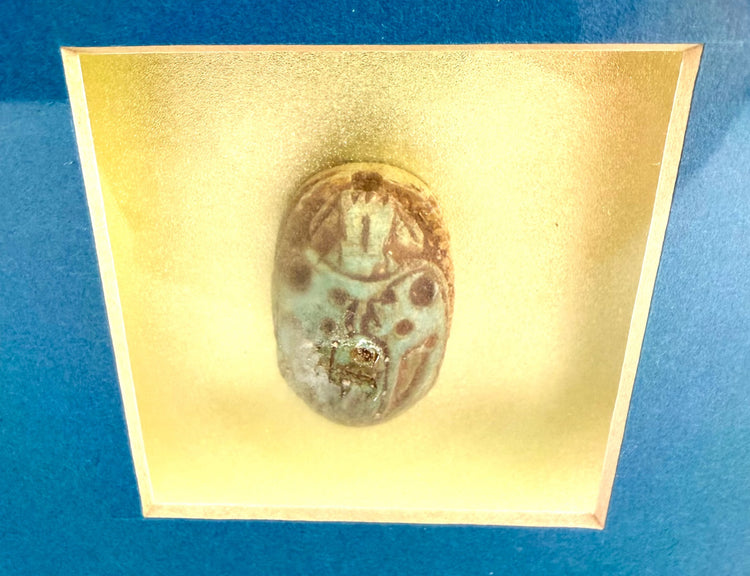 Decorative Egyptian scarab artwork featuring a radiant solar disk, symmetrical winged figures, and traditional symbols of regeneration.