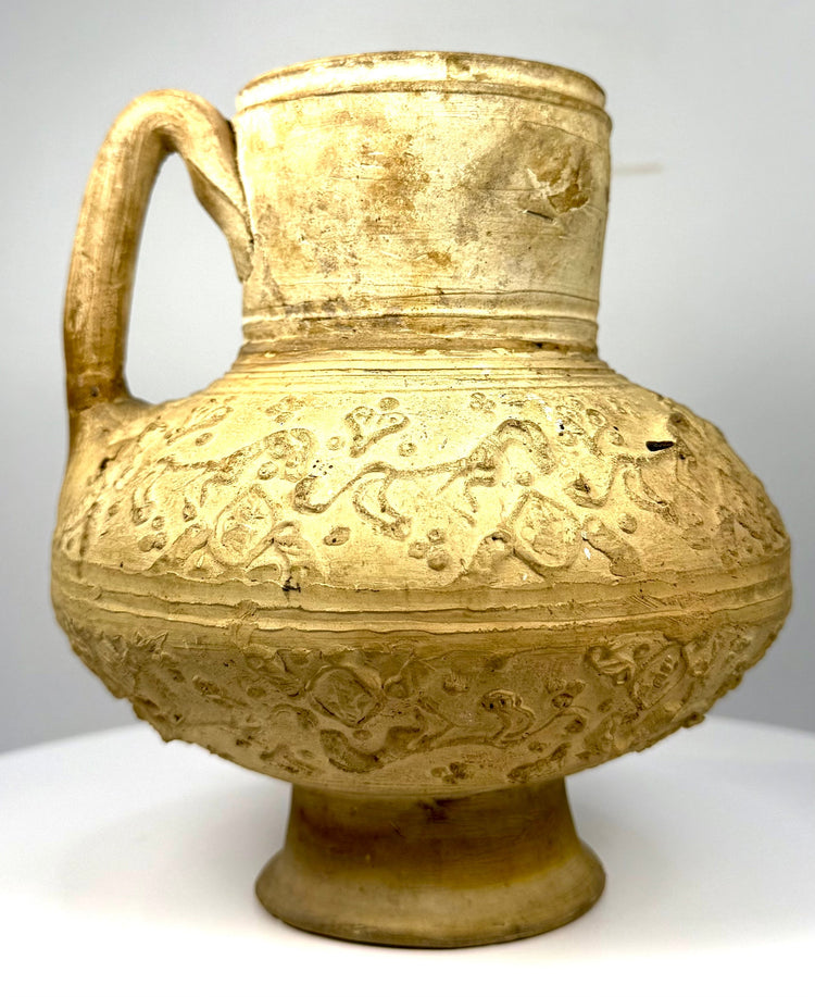 Antique Islamic earthenware pitcher with a broad rounded body, cylindrical neck, flared rim, and intricate moulded ornamentation.