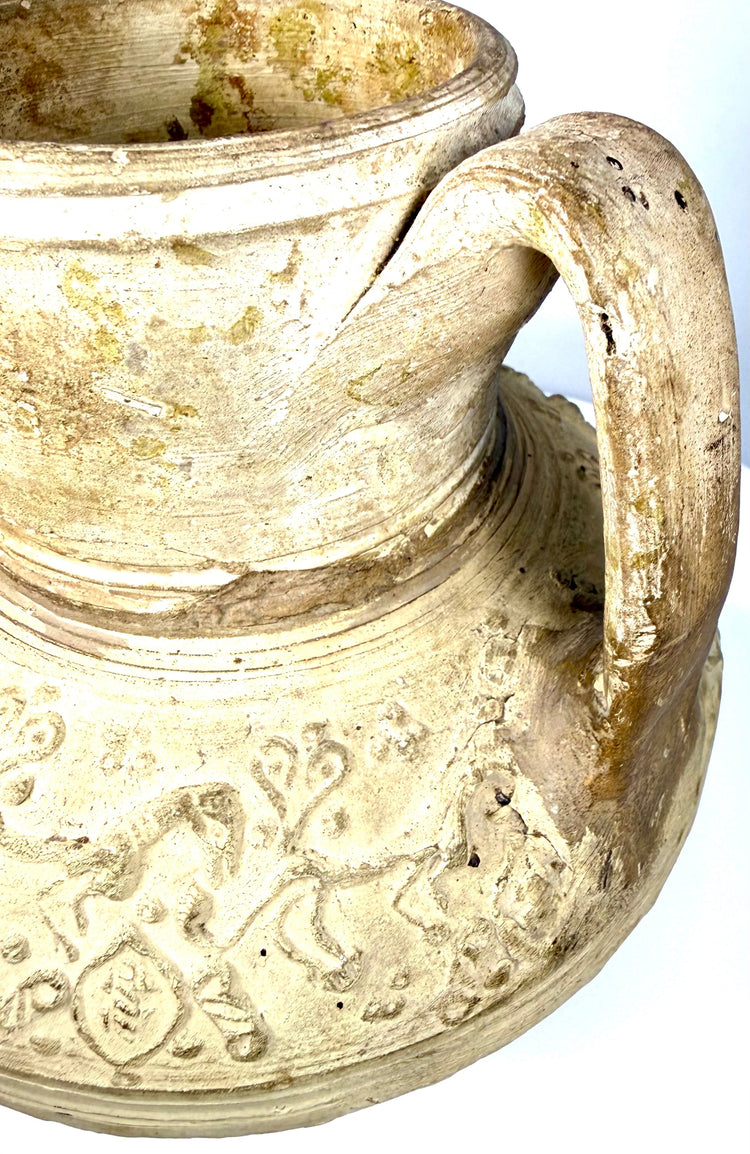 Intricate moulded animal relief on a medieval Islamic pottery pitcher, featuring elongated quadrupeds and decorative circular motifs.