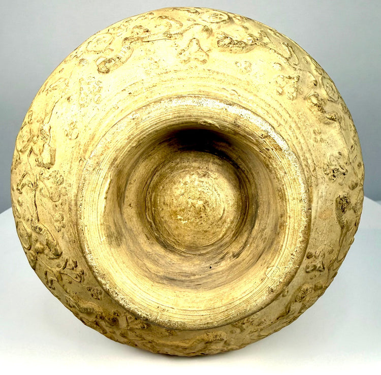 Medieval Persian-style earthenware ewer with a thickened pouring rim, textured buff ceramic surface, raised ornamental relief, and curved handle.
