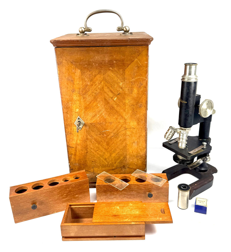 Early 20th-century Spencer laboratory microscope beside its mahogany carrying case, removable wooden storage racks, and optical accessories.