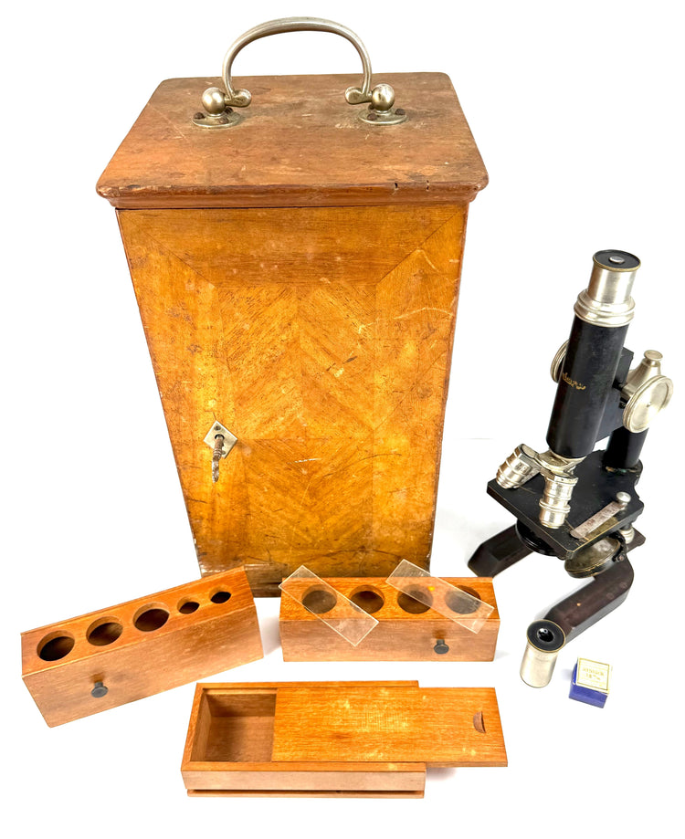 Angled view of an antique Spencer microscope collection featuring a tall wooden carrying cabinet, objective storage racks, and slide box.