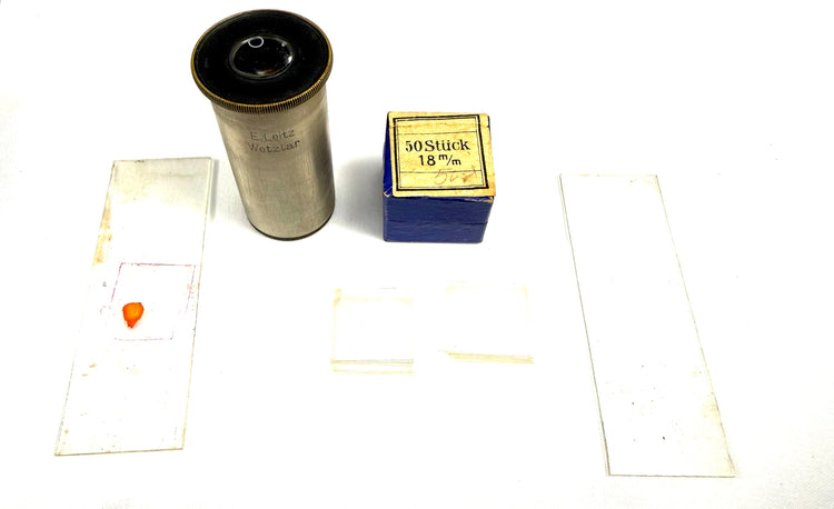 Assorted antique microscope accessories including glass specimen slides, optical components, and period scientific packaging displayed together.
