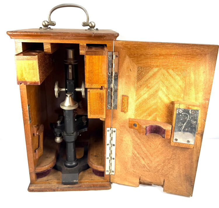 Open antique wooden microscope cabinet revealing the Spencer compound microscope secured inside, with fitted compartments and storage racks.
