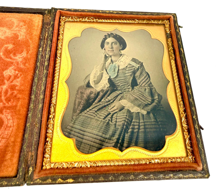 Early American cased photograph showing an elegantly dressed woman resting her head against one hand, with decorative velvet interior.