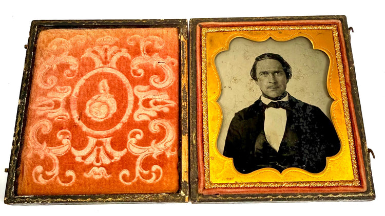 Open Victorian photographic case featuring a seated gentleman's portrait beside reddish-orange velvet lining with decorative floral motifs.