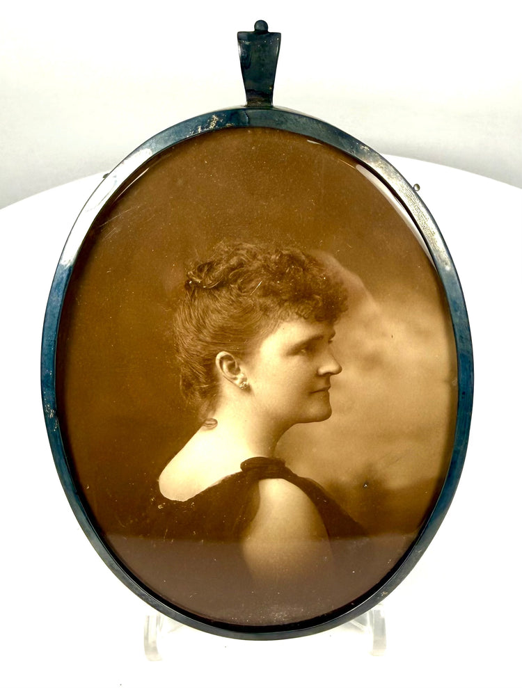 Removable oval sepia photographic portrait of a Victorian woman facing right, wearing a dark formal gown and elaborate upswept hairstyle.