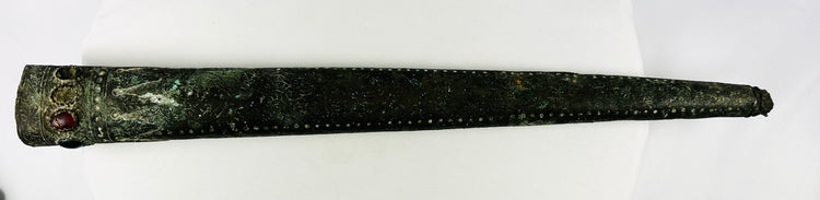 Full side view of engraved Etruscan bronze sword sheath showing dotted repoussé details and gemstone inlays – 9th–7th century BCE artifact with aged patina