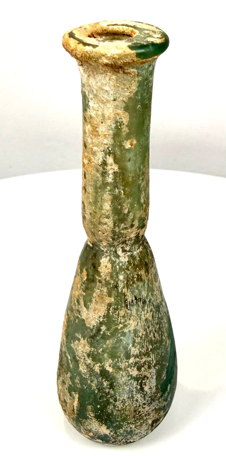 Ancient Roman blown-glass perfume bottle with a weathered exterior, localized pitting, and textured mineral accretions.