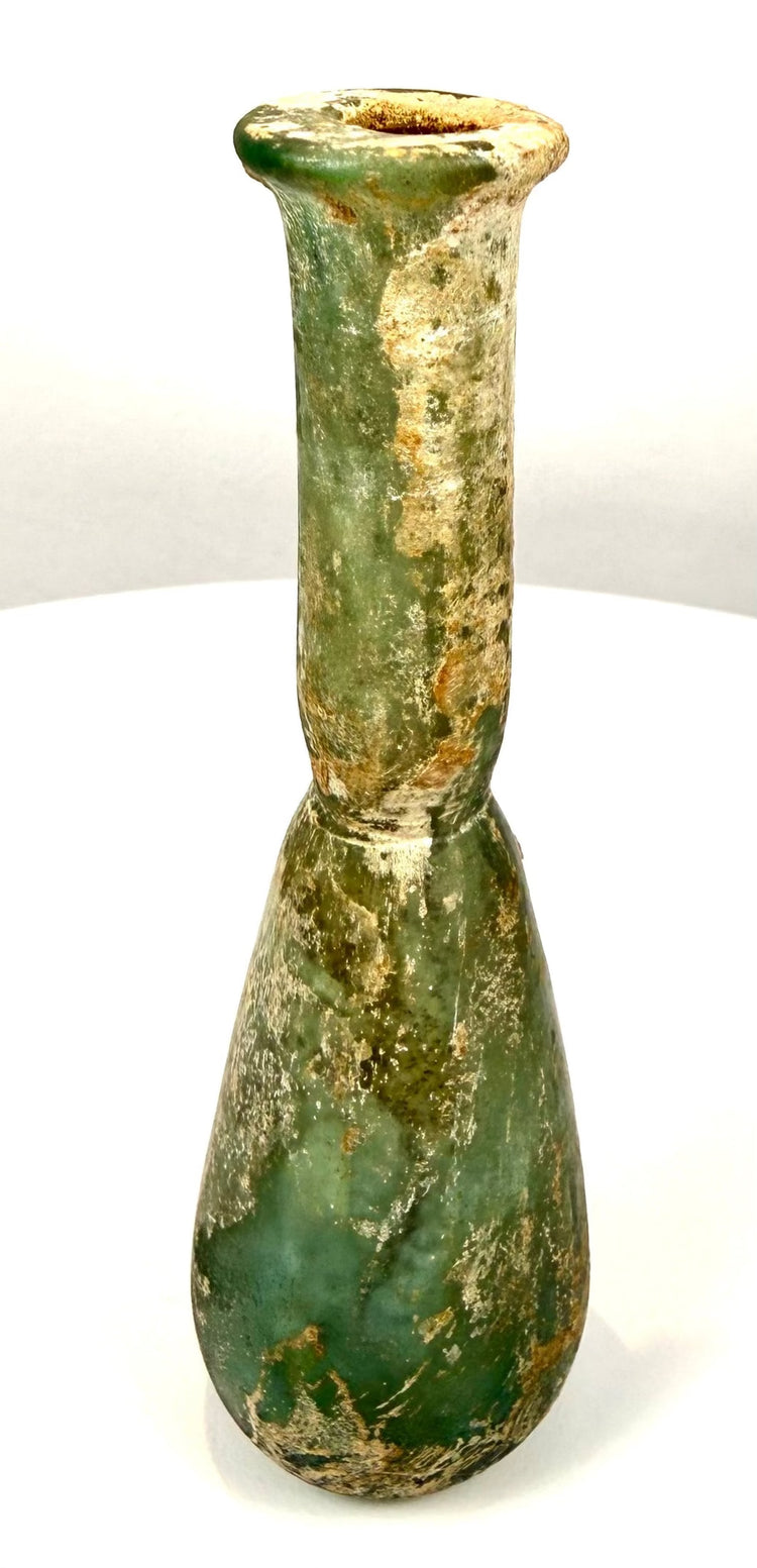 Ancient Roman perfume vessel featuring uneven cream and earthy mineral deposits contrasting with exposed green glass.