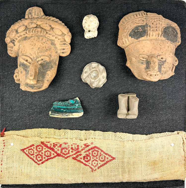 Pre-Columbian shadowbox with terracotta fragments, figurines, and red patterned textile on white background