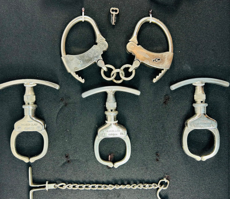 Close-up of antique 19th–20th century iron handcuffs and wrist restraints with original keys, displayed on a dark fabric background.