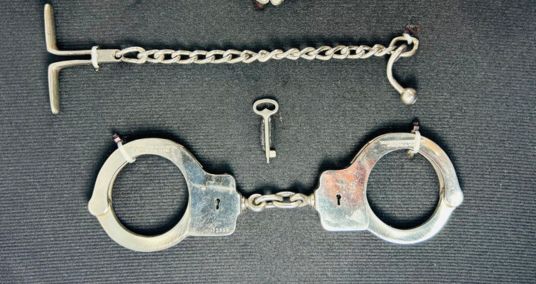 Close-up of antique 19th–20th century iron handcuffs and wrist restraints with original keys, displayed on a dark fabric background.