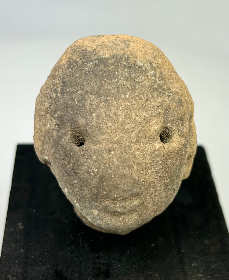 Early Pre-Columbian terracotta head fragment with rounded facial features and drilled eyes, West Mexico, displayed on black stand, 300 BCE–300 CE