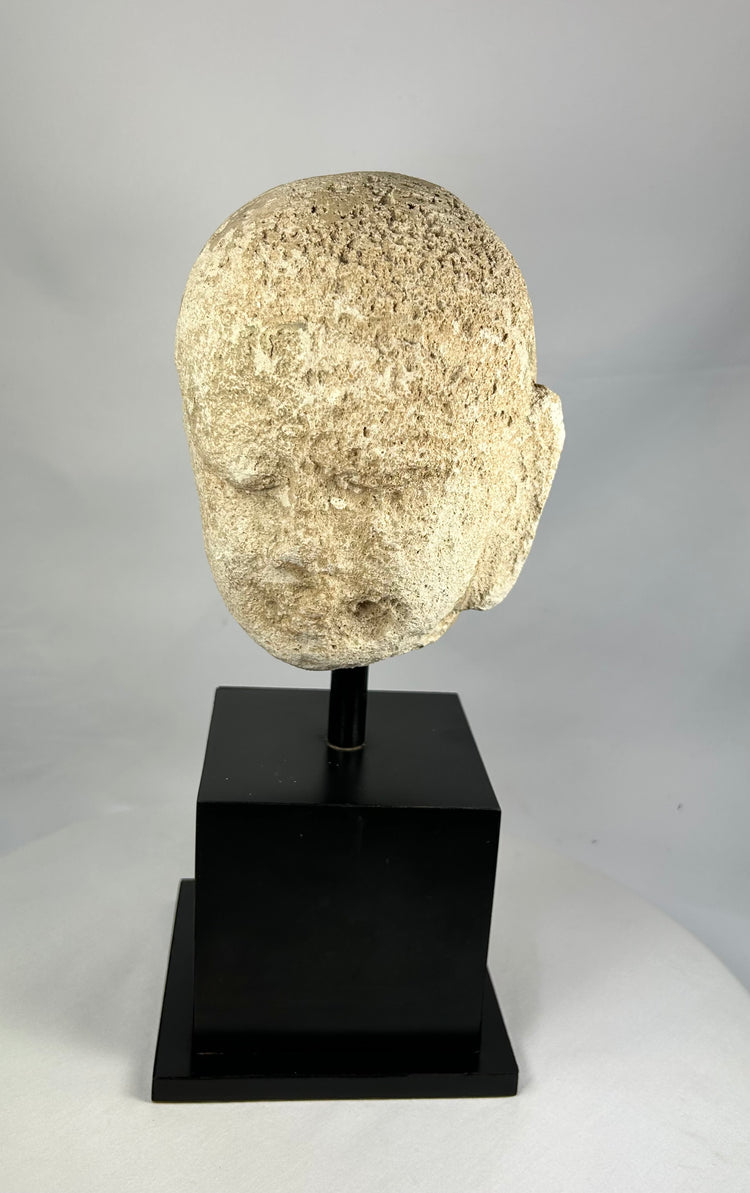 Detailed macro image of Southeast Asian stone Buddha sculpture, 13th–14th century head fragment with meditative features and soft carving lines.