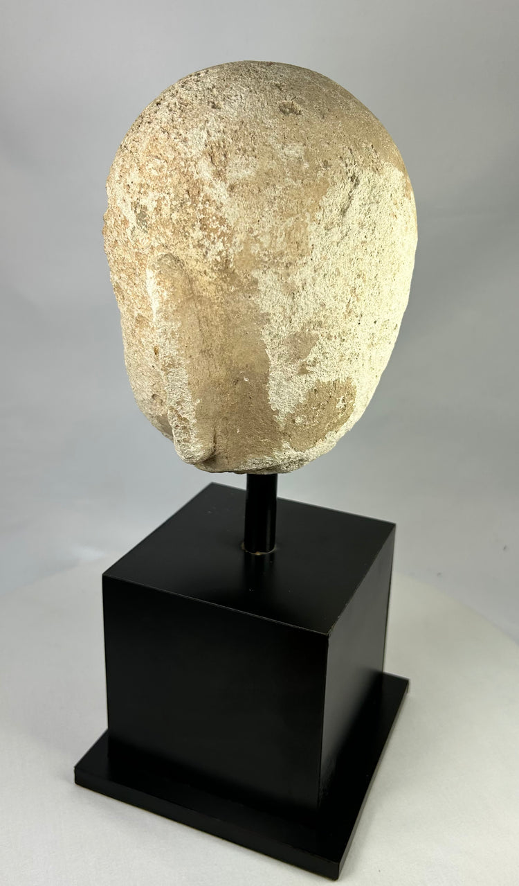 Rear view of ancient carved stone Buddha head from Southeast Asia, 13th–14th century, showing textured surface and aged stone patina.