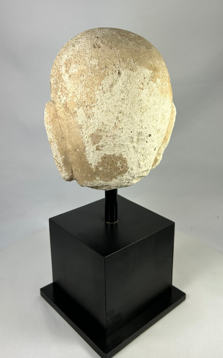 Rear view of ancient carved stone Buddha head from Southeast Asia, 13th–14th century, showing textured surface and aged stone patina.