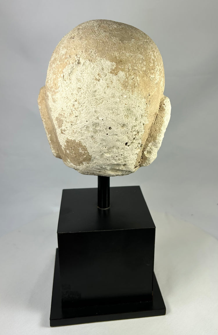 Rear view of ancient carved stone Buddha head from Southeast Asia, 13th–14th century, showing textured surface and aged stone patina.
