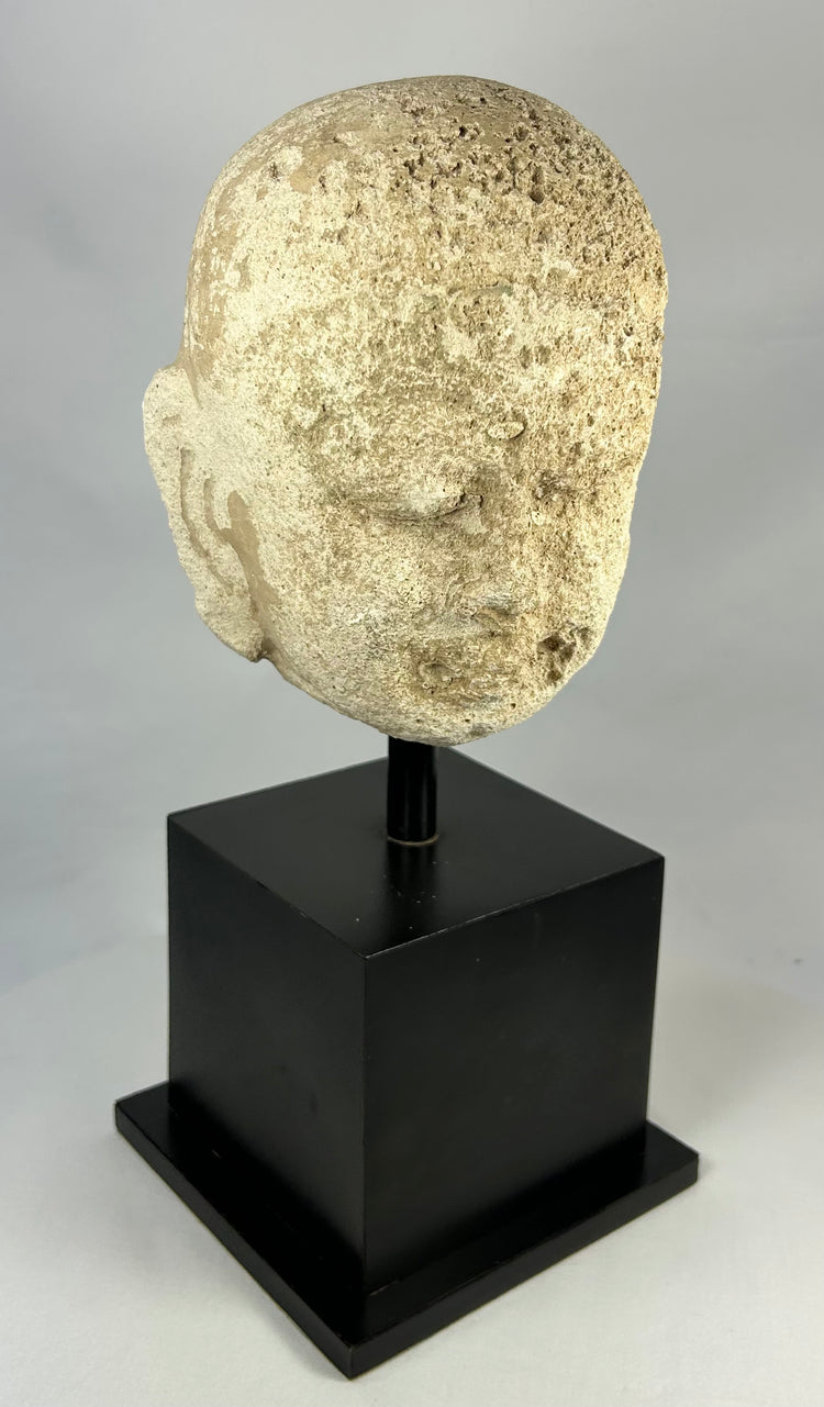 Southeast Asian carved stone Buddha head with serene expression and closed eyes, 13th–14th century, Burma or Thailand, mounted on black display stand.