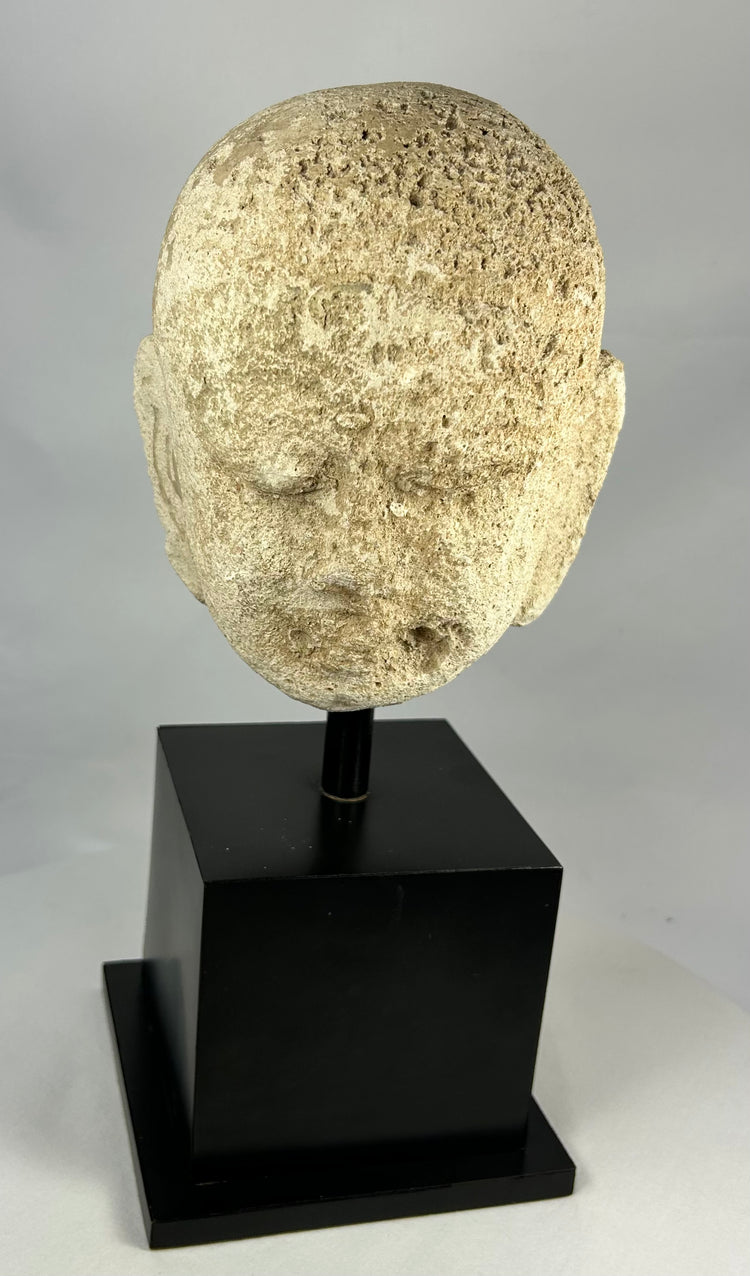 Southeast Asian carved stone Buddha head with serene expression and closed eyes, 13th–14th century, Burma or Thailand, mounted on black display stand.